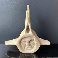 Front view of circular shaman face carved into vertebra