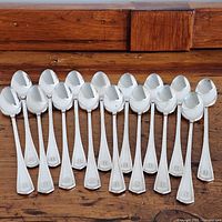 Top-down view of 16 silverplate iced tea spoons arranged side by side showing the handle design and emblem.