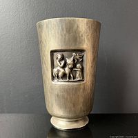Front view of the hammered silvered bronze cup with raised relief panel depicting figures and an animal.