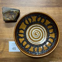Top view of the West German pottery shallow bowl and the ceramic on rock art piece beside it on a wooden surface.