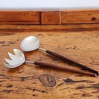 Pair of salad servers laying on a wooden surface, showing the fork and spoon heads with wooden handles