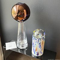 Both vases side by side on black surface against gray wall with lot tag