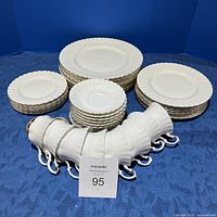 Full set of dinner plates, salad plates, bread plates, cups and saucers arranged on blue backdrop.