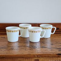 Set of four Pyrex coffee mugs showing front views of mugs and Butterfly Gold gold decal with floral and butterfly pattern around rim