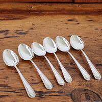 Photo of 6 teaspoons arranged in a row on a wooden surface, all spoons facing up showing bowl