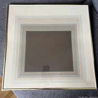 Framed serigraph artwork showing concentric squares in multiple shades of grey and beige with a dark brown center square. Signed in lower right corner.