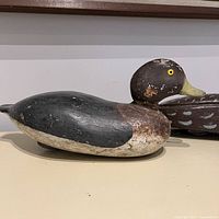 Side profile of the wooden duck decoy showing black, brown and white paint with visible wear and patina.