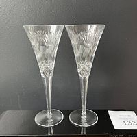 Pair of Waterford crystal toasting glasses with cut etched Millennium Prosperity pattern standing upright on a reflective surface against a plain gray background.