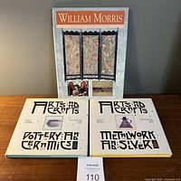 Four hardcover books related to William Morris and Arts and Crafts movement with art deco style fonts and illustrated covers on a wooden surface against a gray wall.