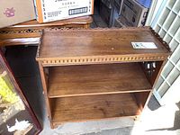 Front view of solid wood bookshelf showing two shelves, carved top edge, and wear marks.