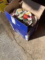 Photo of a large cardboard box filled with numerous buttons in plastic bags and loose, showing general quantity and packaging of the lot.