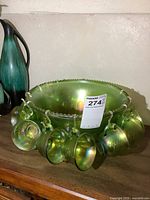 Green carnival glass punch bowl with 12 matching cups hanging from rim, showing shiny, iridescent surface and ribs inside bowl