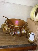 Full set of iridescent carnival glass punch bowl, cups hung on rim, ladle inside bowl, and additional cups stacked.