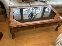 Full view of wood coffee table with smoked glass top showing floral inset design and claw feet.