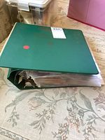Green three-ring binder on floral print fabric surface with visible wear and bulging from contents inside