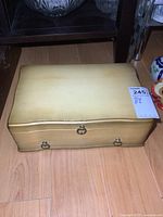 Closed view of vintage wooden chest painted yellow with brass hardware sitting on wooden floor.