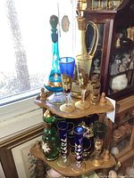 Photo of four glass decanters on two wooden corner shelves, showing decorative floral and gold paint details, various glasses, and bud vases.