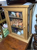 Front view of wooden display cabinet containing small clay pots and porcelain figurines inside.