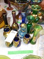 Photo showing collection of blue, green, and amethyst glass vases with gold accents and floral painted designs on a table.