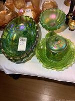 Two large green carnival glass oval fruit bowls with footed bases, a biscuit jar with lid on a fluted plate, and a pedestal candy dish all displayed together showing iridescent green hues and intricate pressed decoration.