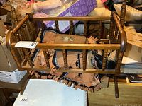 Wooden doll cradle with dolls and photo album inside, showing front view of cradle and contents.