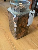Front view of a clear square glass jar filled with pennies, showing the jar's size and content density.