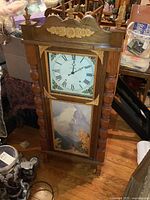 Front view of the large wooden ogee style clock showing painted clock face and scenic landscape panel below.