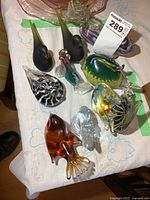 Full view of various heavy art glass figurines on table including birds and fish, showing different colors and patterns