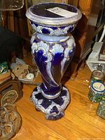 Porcelain pedestal with blue and white detailed patterns on a wooden floor, showing full height and styling.