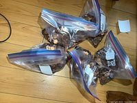 Five large Ziplock bags filled with copper pennies on a wooden floor showing the bulk quantity and bag conditions.