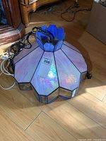 Top view showing purple-pink iridescent stained glass panels with attached black chain lying on wooden floor.