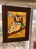 Stained glass owl artwork hanging in window, showing full piece in rustic wood frame.