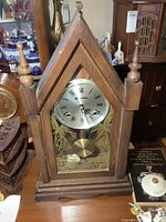 Front view of vintage wooden steeple clock showing clock face, etched glass design and finial details.