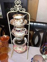 Stack of four unique Royal Albert bone china tea cup and saucer sets arranged vertically suspended from white twisted metal rack with heart detail top