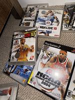Photo showing multiple sports video game cases including NBA Live 10, Madden NFL, NBA 2K10, and NCAA March Madness 2004, indicating titles for PlayStation 2 and PlayStation 3.