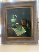Still life painting in dark wood frame featuring jug, pipe, book, and other objects on a table.