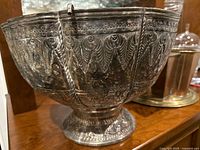 Close-up of one large metal embossed wine chiller showing detailed floral and geometric patterns on a reflective silver-toned surface.