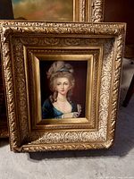 Frontal view of ornate framed portrait painting of a noblewoman with powdered hair and pearl necklace.