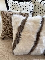 Pillows arranged on carpet, showing black and white spotted pillows, brown animal print pillow, and white furry pillow with brown stripes.