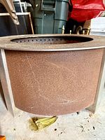 Side view of the large fire pit showing rusted cylindrical body and part of the brass rim