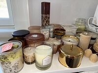 Various candles in glass jars of different sizes, colors, and fragrances, arranged on a white surface.