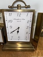 Close-up of front of brass clock showing white face, black hands and numerals, brand name Mclaughlin & Scott, ESTD 1972.