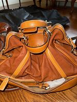 Cognac leather duffle bag opened to show gathered side pocket and double zipper closure