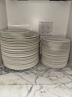 Stacks of white plates and bowls on a marble counter, showing quantity and size differences