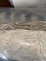 Photo of cream and beige textured fabric bolt with an abstract pattern under protective plastic.