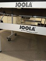 Front frame of table showing JOOLA logo and white metal legs with wheels.