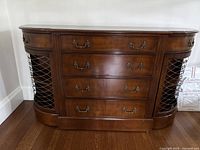 Front view of wooden side cabinet showing the curved sides with metal lattice cane doors and four central drawers with metal handles.