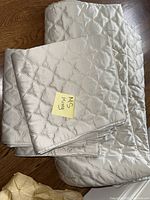 Folded cream quilted coverlet atop matching shams with ‘King’ note