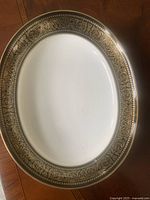 Oval serving dish with white center and wide black border decorated with intricate gold floral and scroll patterns