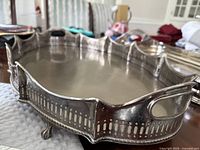 Close-up of the large metal serving tray's decorative cut side and feet, showing silver-tone metal finish.